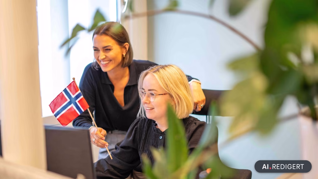 To ansatte som ser på en dataskjerm. Den ene personen holder et norskt flagg.