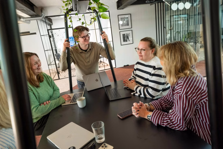 Fire kolleger i tur.digital som snakker sammen rundt et bord.