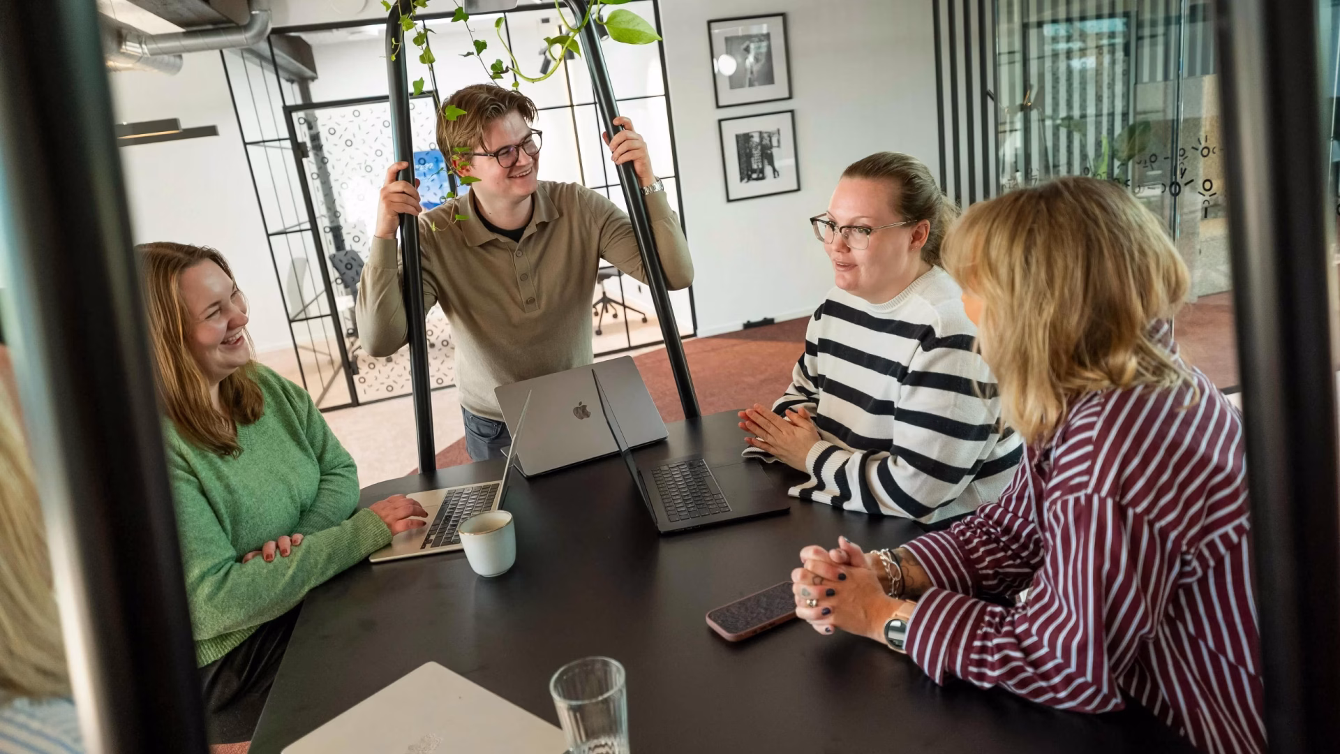 Fire kolleger i tur.digital som snakker sammen rundt et bord.